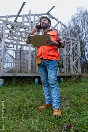 Construction engineer or architect talking on the phone while holding a digital tablet at a building site