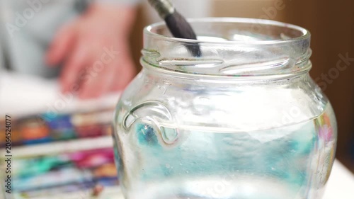  Washing paintbrush in a glass jar filled with water.