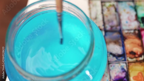  Washing paintbrush in a glass jar filled with water.