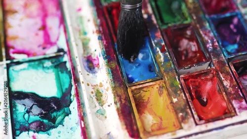 lose up of paintbrush dipping into blue watercolor paint pan.