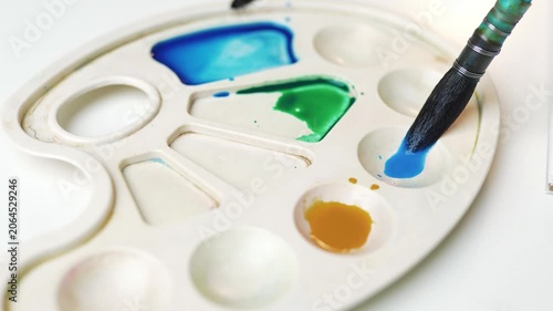 Artist using paintbrush to mix orange watercolor paint on palette.