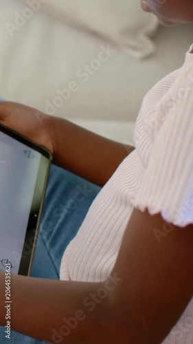 Vertical video: Adjusting grip after tablet tilt, kid in pink top viewing tablet on home sofa