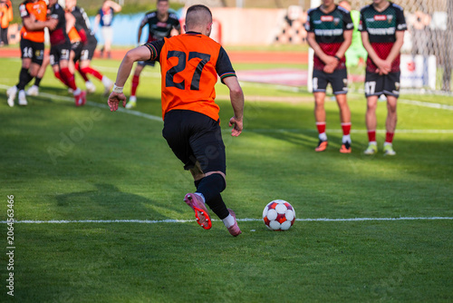 Obraz na plátně A soccer player in an orange jersey with number 27 runs with the ball toward the opponent's free kick wall during a match