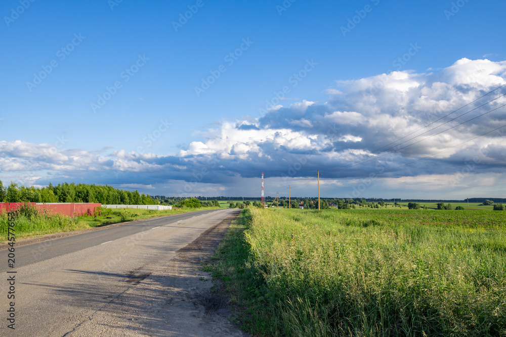 Fototapeta premium Gravel road winds through open fields under bright blue sky