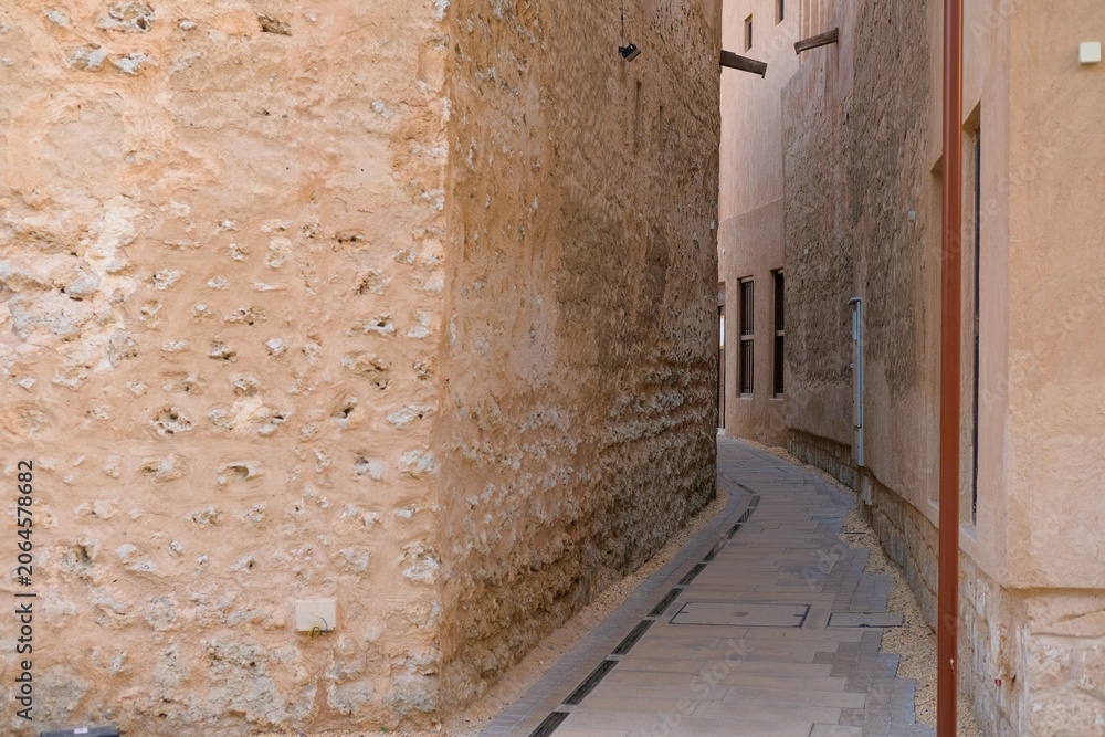Obraz premium Narrow pedestrian street lined with traditional buildings in UAE. Historic architecture, textured walls and heritage urban environment.
