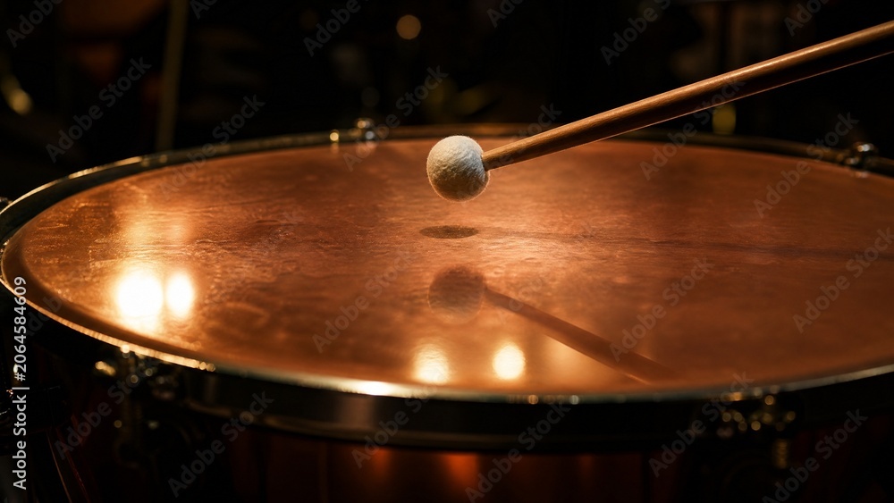 Obraz premium Close-up of a timpani drumhead with a drumstick poised just above its center.