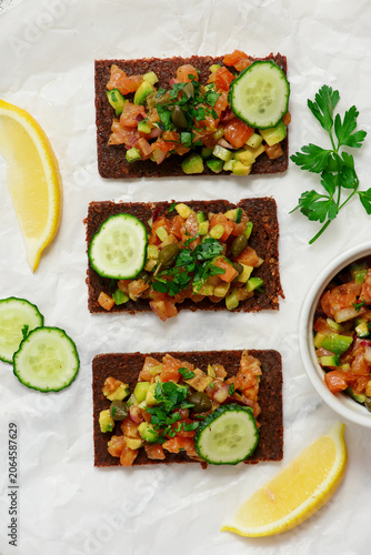 Salmon tartare with avocado and cucumber on pumpernickel rye bread.