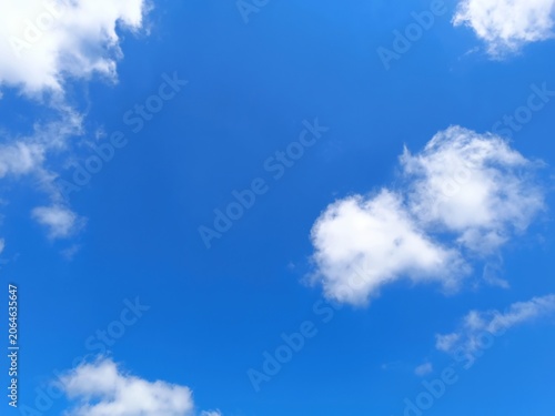 Scattered small white fluffy clouds in a clear blue sky. Sunny summer weather background with copy space