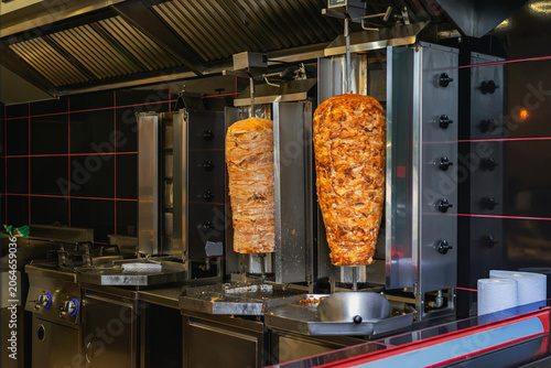 Shawarma meat rotates on vertical grills in fast food kitchen, with shawarma equipment, steel counter ready for service. Concept of kebab cooking, street restaurant prep, takeaway menu, food business