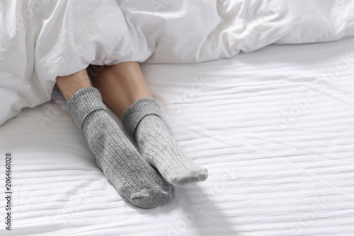 Woman in warm grey socks on her feet lying in cozy bed, closeup. Space for text