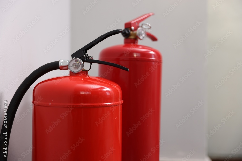 Obraz premium Two red fire extinguishers near white wall indoors, closeup