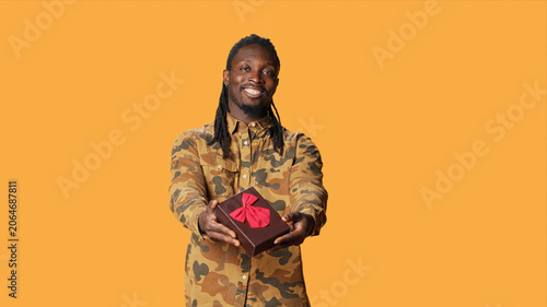 Tableau sur toile African American person offering giftbox to his girlfriend, giving present packed with ribbon and bow on camera, with young adult doing cute romantic gesture on their anniversary or valentines day