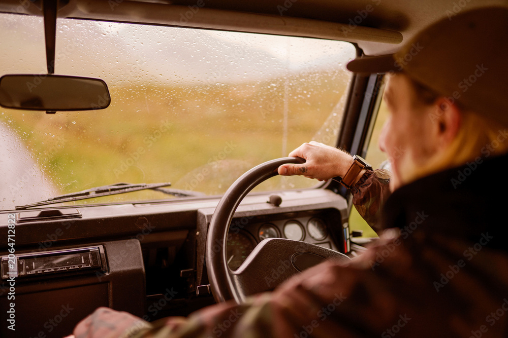 Fototapeta premium Man driving vintage car through rainy countryside