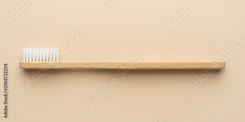 Flat lay of a natural bamboo toothbrush with white bristles on a beige background