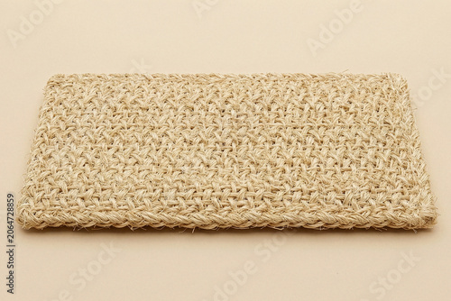 Rectangular woven natural fiber mat on a beige background