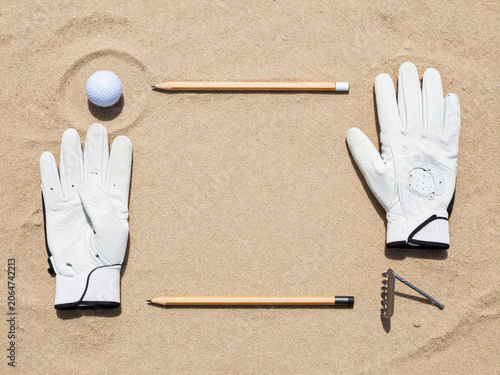 Golf Accessories Stock Layout Golf ball, glove, scorecard pencil and bunker rake arranged neatly on sand, top-down view, clean commercial stock composition, 