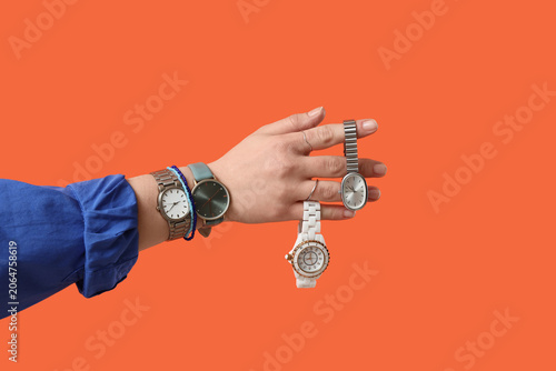 Female hand with stylish wristwatches and bracelets on orange background