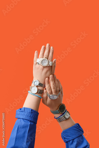 Female hands with different stylish wristwatches and bracelets on orange background