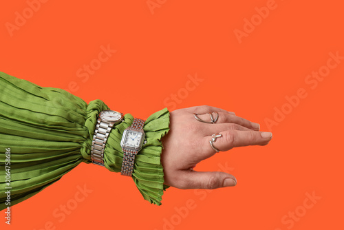 Female hand with stylish wristwatches and rings on orange background