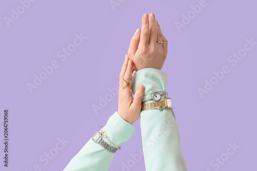 Female hands with different wristwatches and stylish jewellery on purple background