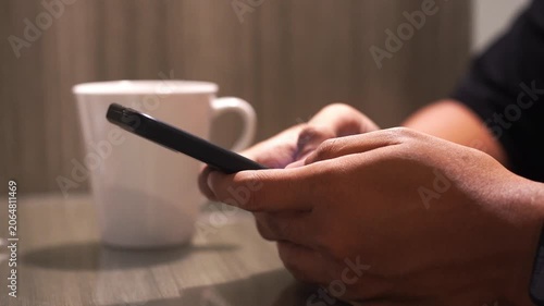 Man drinking hot coffee from white mug sitting at the table and typing text holding mobile phone in the hand. Closeup relax lifestyle video
