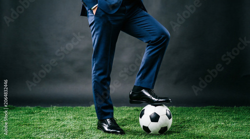 Business suit meets soccer passion as foot rests on ball symbolizing teamwork and determination.