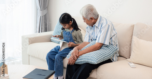 Obraz na plátně Asian grandfather and granddaughter spending time together at home, sharing learning, family love, care, and meaningful intergenerational moments