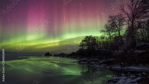 Colorful aurora borealis over frozen coastal landscape at night.