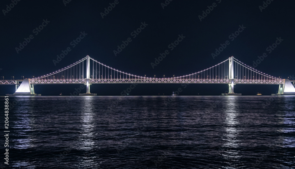 Fototapeta premium Illuminated suspension bridge over the dark sea at night