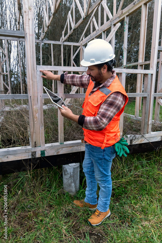 Construction inspector examining a wooden house frame while holding a digital tablet