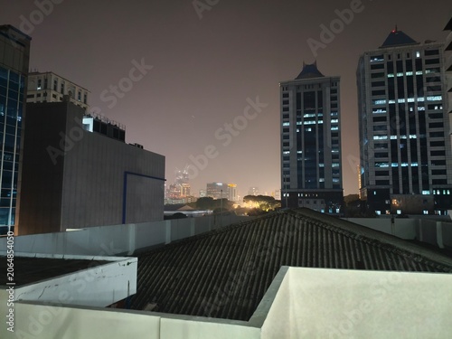 Modern City Skyline at Night with Illuminated Skyscrapers and Rooftops