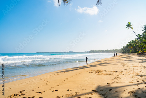 Distant view of female traveler walking alone on a pristine tropical beach.