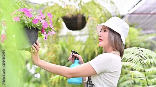 Cheerful Female Florist Spray Water On Pink Flower Pot In Green Garden