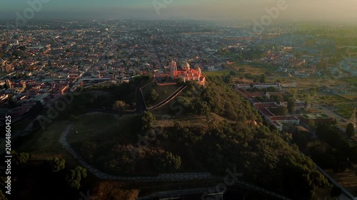 Aerial drone slowly ascends over the Cholula pyramid and its hilltop church at dawn, revealing the Pueblo Magico town spreading beneath in a sweeping cinematic composition with no people present