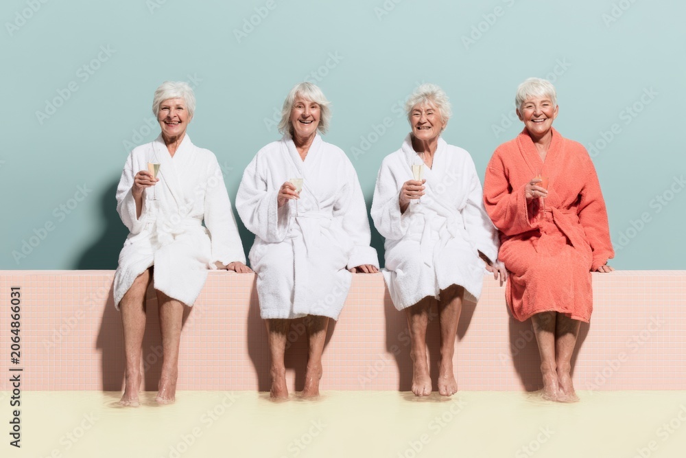 Obraz premium Four senior women in plush robes celebrate and toast with champagne flutes while sitting at a spa pool, for friendship and wellness lifestyle content