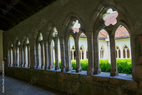 Foto Old stone cloister arcade with arched openings revealing a tranquil courtyard an