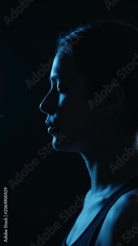 Silhouette of young woman illuminated by cool blue light in the dark. Vertical video
