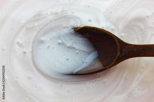 Fotografi a thick, clear white cosmetic gel texture in a container, with a wooden spoon im