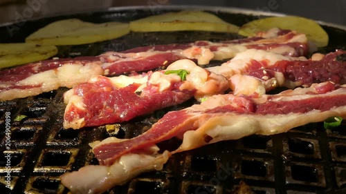 Juicy marinated beef slices sizzle on a Korean BBQ grill with golden potato slices, sesame seeds and fresh green scallions scattered atop