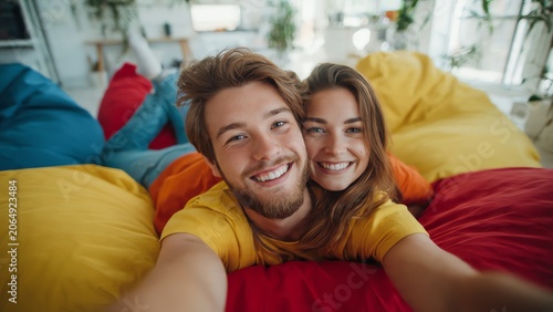 Happy couple taking selfie on colorful bean bags in cozy living room