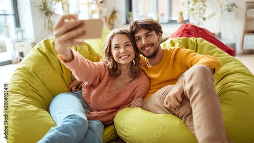 Happy couple taking selfie on colorful bean bags in cozy living room