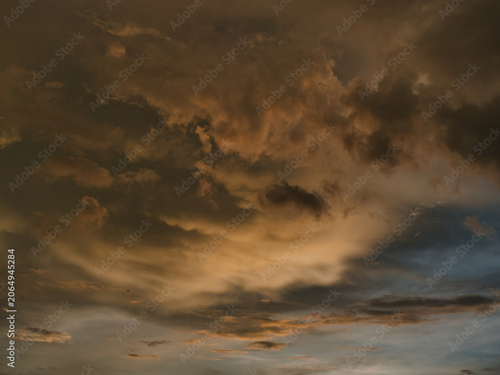 Obraz premium Sunset sky was beautiful, with thick, dark orange and golden clouds near the horizon and dark, warm-toned clouds turning cool blue at the bottom.