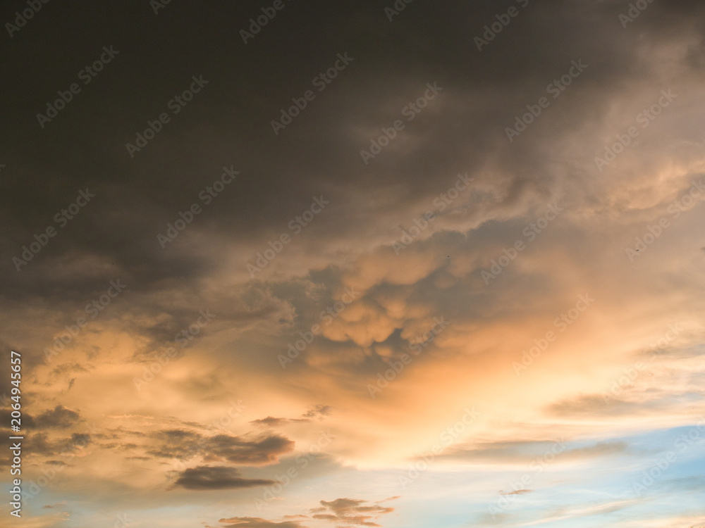 Obraz premium Sunset sky was beautiful, with thick, dark orange and golden clouds near the horizon and dark, warm-toned clouds turning cool blue at the bottom.