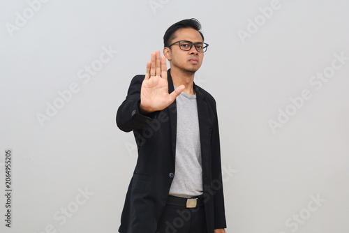 A young, unhappy looking businessman raises his hand towards the camera, making a gesture of prohibition, restricting something, looking serious, a warning expression.