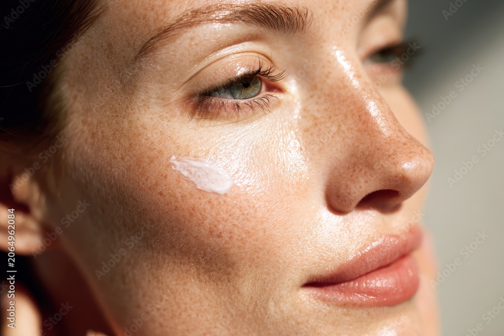 Fototapeta premium Radiant Skin Texture: A close-up profile shot of a woman's face, showcasing her skin's natural texture with a subtle application of cream, illuminated by soft sunlight.