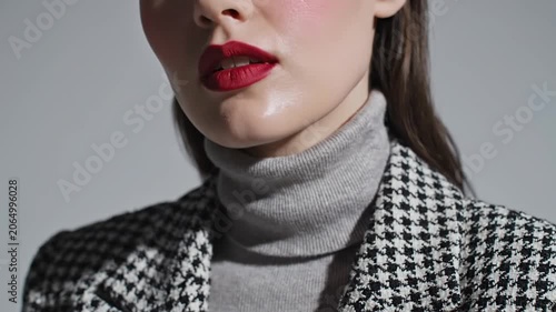 Young woman with red lipstick wearing houndstooth blazer and grey turtleneck in studio