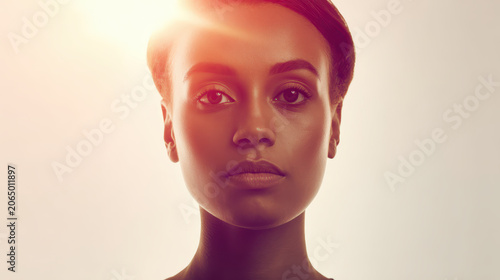 Close-up portrait of a young woman with dark skin, illuminated by a warm, golden light that casts a gentle glow on her face, conveying a sense of serene beauty and inner strength.
