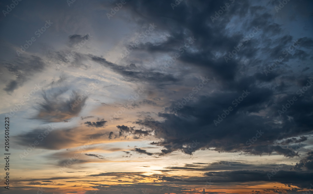 Fototapeta premium Dramatic Sunset Sky Background, Dark Storm Clouds Mixing with Golden Evening Light and Wispy Formations.