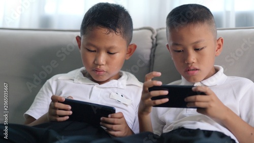 Bild auf Leinwand Two Asian boys holding modern smartphones for interactive multiplayer gaming