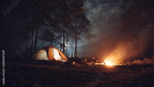 Night camping in forest with illuminated orange tent and glowing campfire